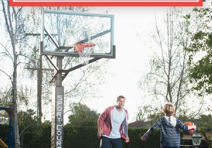 Two men playing basketball on a court with trees in the background.